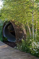 Leucanthemum vulgare - Ox-eye daisies and Betula pendula - Silver Birch - and a woven willow arch covering a large water pip Tomatoes, aubergine and chillies in timber framed raised bed - The Thames Water Flourishing Future Garden - RHS Hampton Court Palace Garden Festival 2019 - Designer: Tom Woods