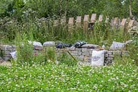 Acurved dry stone bench backed with timber palisade surrounded by flowering perennials - The BBC Spring Watch Garden at RHS Hampton Court Festival - Design: Jo Thompson in consultation with Kate Bradbury