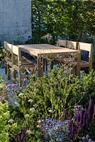 Timber table and chairs on slab patio - The Viking Cruises Lagom Garden at RHS Hampton Court Palace Garden Festival 2019 
