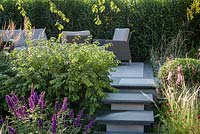 Stone steps leading to raised patio with outdoor sofa and armchairs -APL - A Place To Meet Garden - Hampton Court Palace Garden Festival 2019  
Designer: Cherry Carmen