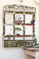 A recycled piece of timber furniture with peeling paint mounted on a wall decorated with metal figures and a handmade shell mobile.