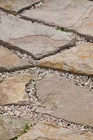 Gaps in irregular shaped sandstone paving mulched with small seashells.