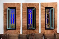 Tall narrow windows with ornate metalwork grille and bright blue wall behind, cushions on chair in front. Le Jardin Majorelle, Majorelle Garden, Marrakech