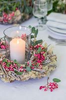 Pillar candle in storm lantern surrounded by wooden wreath with moss, rowan berries and Eucalyptus