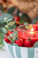 Table decoration comprising red candle in dish with rosehips and Eucalyptus foliage