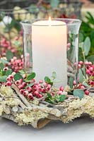 Table decoration, pillar candle in storm glass surrounded by wooden wreath decorated with pink Sorbus - Rowan - berries amd Eucalyptus foliage