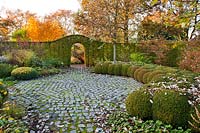 Paved area surround by topiary Buxus - box balls and with a path under archway cut into Carpinus betulus  - hornbeam hedge