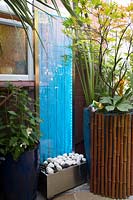 Water feature by house in a small town garden with tropical foliage plants