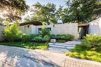 Limestone path between beds of foliage plants to contemporary house, raised beds of steel by house wall with Agave
