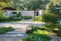 Front garden of a contemporary house, limestone shallow steps and path with beds of foliage plants either side. Steel raised beds of Agave near house wall