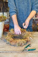 Man wiring moss to wire frame to from base of wreath