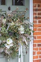 Finished white themed wreath with feathers hanging on sage green door of cottage