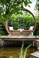 Wooden seating deck with cushions above pond - Stop and Pause Garden - RHS Hampton Court  Palace Garden Festival 2019  