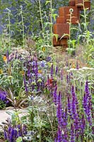 Purple Salvia sylvestris 'Mainacht', Echinops  and Eryngium planum sea holly with  Fennel with detail of  in front of 'Honesty' sculpture in Corten steel by Jill Clarke - The Lower Barn Farm Outdoor Living Garden - RHS Hampton Court  Palace Garden Festival 2019 
