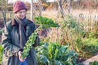 Woman holding a harvested stalk of Brussel Sprouts 'Trafalgar'. 