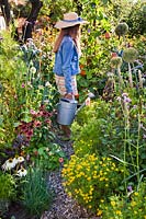 Girl with a watering can. Mixed beds with Echinacea 'White Swan', Tagetes tenuifolia, Rudbeckia hirta, Tropaeolum majus, Allium schoenoprasum, Lavatera trimestris, Ocimum basilicum.
