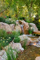 A waterfallconstructed from large boulders and small rocks, interplanted with a variety of flowering and strappy leaved plants 