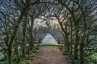 View from under trained arch of apple trees to formal garden at Fittleworth House garden, West Sussex, UK.