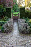 View of brick path, Yew hedge and garden gate in large Surrey Garden 
