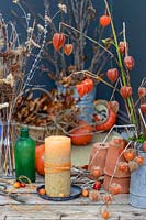 Candle with string decoration on metal tray, with crab apples, gourds, dried flowerheads and Physalis