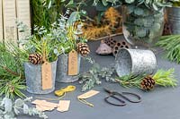 Name tags hung from metal pots filled with mixed green foliage and pine cones