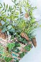 Woven basket with a mix of foliage hanging in hallway ready for use at Christmas