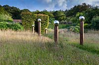 Avenue of stainless steel globes mounted on posts of varying height in the Meadow. Veddw House Garden, Monmouthshire, Wales, UK.