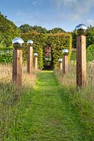 Avenue of stainless steel globes mounted on posts of varying height in the Meadow. Veddw House Garden, Monmouthshire, Wales, UK.
