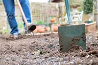 Garden spade in a vegetable garden in front of a gardener turning the soil over in early spring