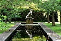 View along canal to sculpture of a seated dog on plinth with hedge backdrop and Pyrus calleryana 'Chanticleer' trees either side