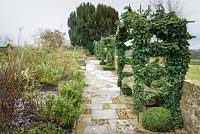 View along paved path with arbour coated in Hedera - Ivy - with bench
