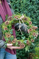 Woman holding finished wreath made with Ivy, Cones, Moss, Holly and Yew