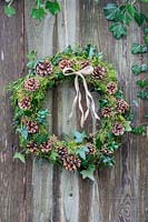 Finished wreath made with Ivy, Cones, Moss, Holly and Yew hanging on rustic wooden door outside