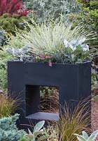 A black, contemporary planter set within the landscape, planted with a monochromatic, deer resistant, drought tolerant selection of shrubs, perennials and annuals.