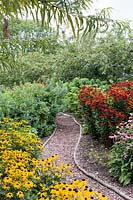 A narrow path, edged with marine rope meanders through a border of golden Rudbeckia fulgida var. sullivantii 'Goldsturm', deep red Helenium and pink Echinacea at RHS Harlow Carr