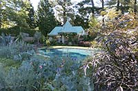 Chanticleer Garden: Turqouise blue swimming pool and pool house with turqouise metal roof. Creative border plantings in shades of silvery-blue and coral