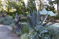 Border with silver-blue colour theme, plants: Agave Americana, Crambe maritima - Sea Kale, with rooster statues alongside path