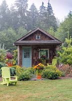 Rustic cabin within a country garden, styled with orange container gardens and chartreuse Adirondack chairs.