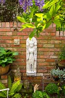 Brick wall with wall plaques and Buddha heads, all displayed alongside containers with Hosta and other perennials 