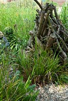 Wood pile in wildlife area of tall grasses to provide shelter for insects and small animals - Open Gardens Day, Wivenhoe, Essex