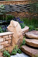 Yorkshire stone used for garden walls and steps, with natural boulder built into wall as a feature and planting of Alchemilla mollis, Irises, Agastache and ferns - RHS Chelsea Flower Show
