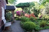 The front of the house in Spring at Brooke Cottage with shrubs trees and perennials including flowering Azalea Rhododendron Buxus and ferns.