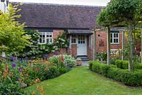 Cottage garden with lawn, wooden pergola and mixed bed planted with Alliums, lupins and Geum 'Totally Tangerine'.