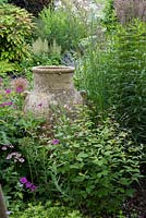Huge urn immersed in border of alliums, stipas, hardy geraniums, astrantias and Gillenia trifoliata.
