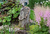 A large chunk of driftwood with string of hagstones stands between ligularias and astilbes