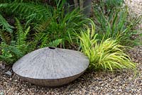 An unusual ceramic pot set amongst ferns and grasses adds interest in a shady corner of a gravel garden.