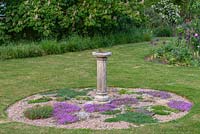A sundial on a stone plinth in the centre of an island bed planted with scented creeping thymes.