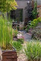 A path is made from wood off-cuts leftover from laying the wooden decks, fixed at equal intervals beneath the gravel. A quiet seating area is outside the studio, to the right a raised bed with euphorbia, black elder and mauve erysimum.