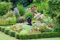 Statue of entwined lovers in a Buxus edged parterre with Rose 'Little White Pet', Rosa 'Kent', and Sedum spectabile. July.