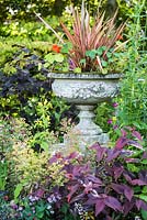 Decorative urn planted with a phormium and nasturtiums in a border.